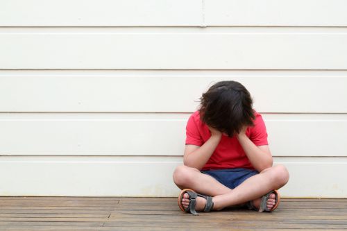 Boy wearing red t shirt and shorts with head in hands