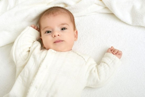 Baby lying on back wearing white baby grow