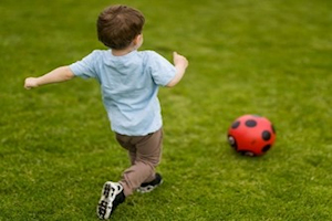 Young boy kicking a red football