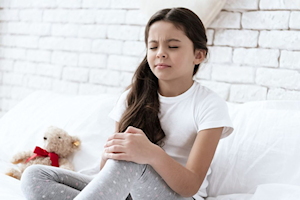 Young girl in white t shirt and leggings holding left knee with eyes closed