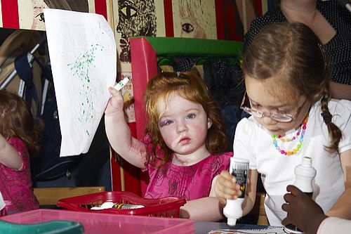 Young girl in pink dress holding up drawing