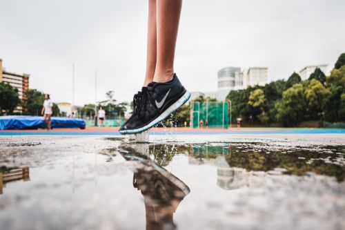 Person in black trainers jumping above a puddle