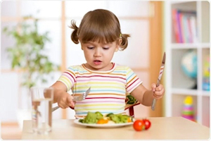 Young child with knife and fork eating a salad