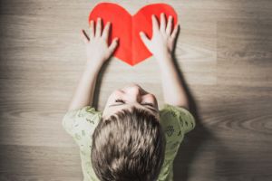 Small child with both hands on a red heart