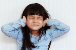 Young girl holding hands over ears with eyes closed