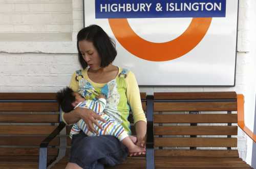 Mother breastfeeding baby sitting on a bench at train station