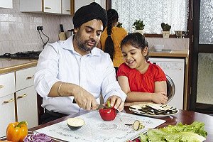 Man in turban showing young girl how to cut a red pepper Man in turban showing young girl how to cut a red pepper